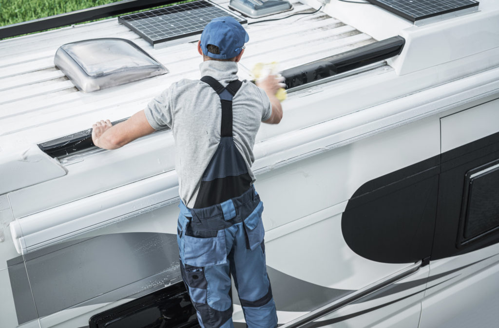 Recreational Vehicles Industry Theme. Caucasian RV Service Worker Washing Camper Van Roof Using Large Soft Sponge and Cleaning Detergent.
